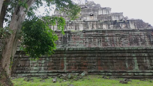 Ancient stone ruins of Koh Ker Pyramid Temple overgrown with moss and trees in Cambodia. The weathered stone blocks show signs of age and the encroaching jungle.