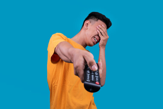 Disappointed Young Indonesian Male Closing His Eyes While Holding TV Remote