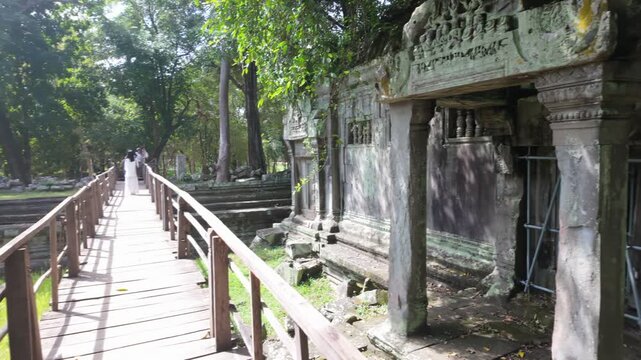 Ancient stone ruins overgrown with moss and vines, featuring intricate carvings and barred windows, in Prasat Beng Mealea, Siem Rep, Cambodia. The weathered facade evokes a sense of history and decay.