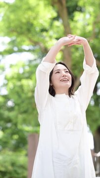 [スロー]自然の中で新緑で深呼吸をしてリフレッシュする女性の健康ライフスタイルイメージの縦動画