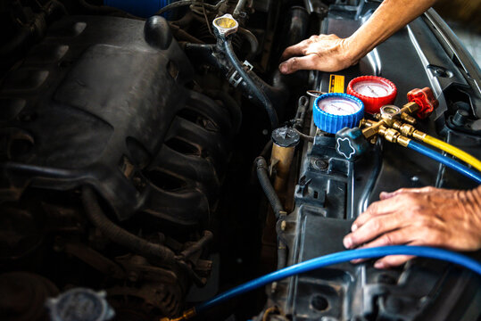 Mechanic checking and refilling car air conditioning system with manifold gauge set in auto repair shop. Vehicle maintenance concept.