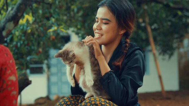 Young Woman Lifting Up Cute Kitten in Village