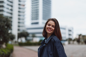 Obraz premium Smiling young woman with dark hair stands in a modern urban plaza, with tall buildings behind, enjoying a bright, carefree moment