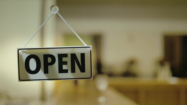 Business owner flipping open sign to closed on glass door as lights turn off in establishment.