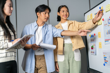 Obraz premium Happy asian business team brainstorming and discussing marketing strategy at whiteboard in office, Smiling female leader presenting data to colleagues, Startup teamwork and corporate planning concept