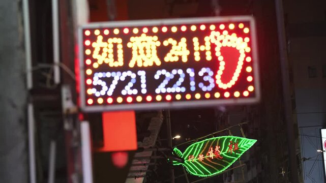 A night view focuses on a traditional neon sign with a blurred modern LED display in the foreground in Hong Kong, China. Illustrates the fading cultural heritage amidst a changing urban streetscape.