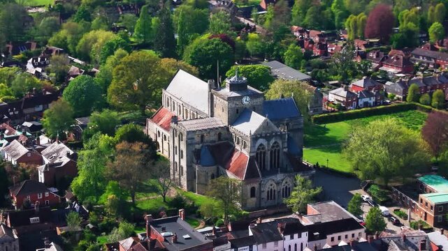 Aerial drone footage of Romsey Abbey in Hampshire, showing the historic abbey church surrounded by trees, green spaces, rooftops, streets, and nearby countryside on a sunny day. Useful for British