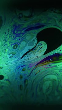 Vertical video. Defocused psychedelic texture. Circling fluid. Green neon blue color paint bubble dark black flow floating on abstract acrylic background.