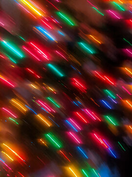 A dynamic, full-frame abstract intentional camera movement (ICM) shot showing vibrant red, green, blue, and gold holiday lights blurred into bright diagonal streaks against a dark background.