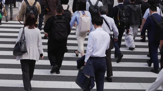 横断歩道を渡り朝の通勤するビジネスマンたちの後ろ姿のスローモーション　東京
