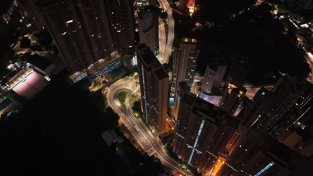 Aerial tracking shot of illuminated high-rise buildings in Hong Kong at night.