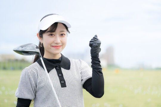 ゴルフ練習場で上達や成功を喜ぶ ガッツポーズの女性のスポーツライフスタイルイメージ　カメラ目線の笑顔