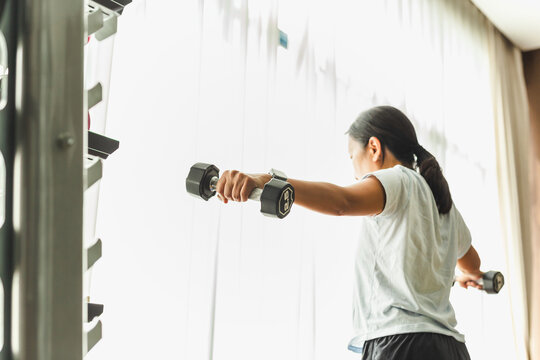 Angled rear view of woman exercise with dumbbell lateral raise at the gym.