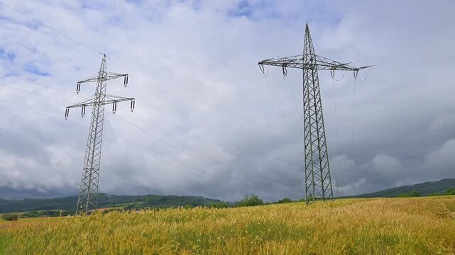Getreidefeld unter einem bew&ouml;lkten Himmel mit dominierenden &Uuml;berlandleitungen, Sommer, Germerode, Geo Naturpark Frau-Holle-Land, Hoher Meissner, Hessen, Deutschland