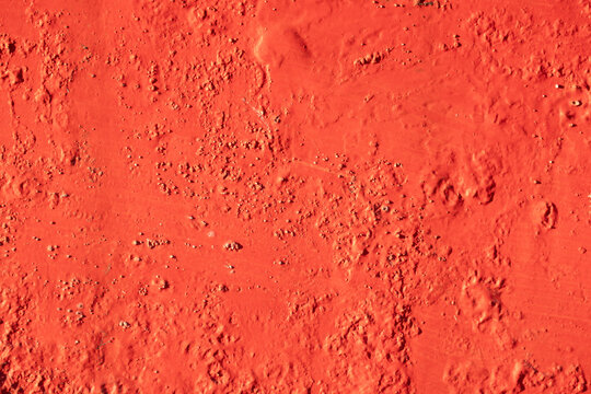 Rough-textured cement or plaster wall painted red. Cracked concrete or plaster with unevenness, chips, and holes.