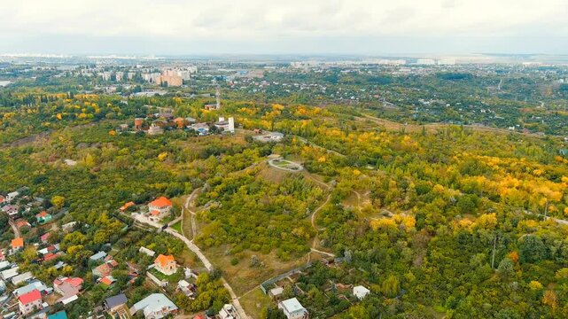 Saratov, Russia. Green Island, Drone footage over dense autumn woodland with a circular hilltop clearing, the Volga riverscape and city skyline visible on the horizon under an overcast sky. Drone foo
