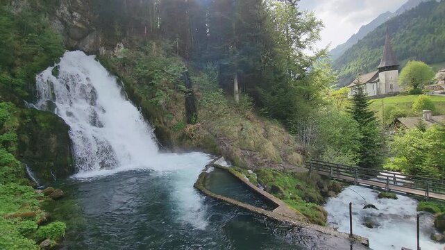 Jaun valley in the canton of Fribourg, Switzerland, idyllic alpine landscape with waterfall and medieval church chapel in the background.