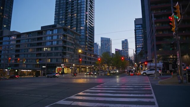 City traffic moving at an urban intersection with modern skyscrapers and traffic lights during twilight hours in downtown Toronto, Ontario, North America