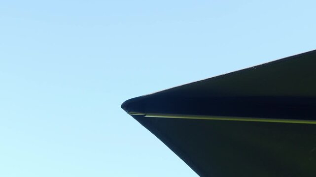 slow motion shot of the big outdoor umbrella corner with view on the blue cloudy sky.
