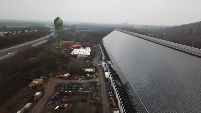 Drone travels parallel to the solar covered industrial facade while birds cross the frame and the camera yaws.