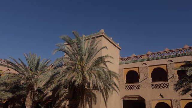 Ornate Moroccan kasbah style building with arched balconies and zellige trim beside tall palm trees