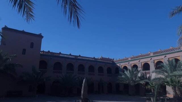 Moroccan kasbah courtyard featuring arched arcades clay walls and palm trees under blue sky