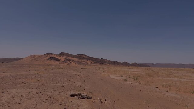 Wide arid desert landscape with low rocky hills sparse scrub and clear blue sky