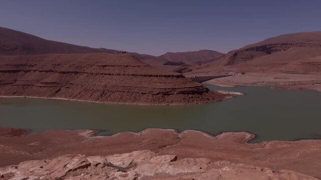 Reservoir with turquoise water and exposed dry shoreline beneath red sedimentary cliffs