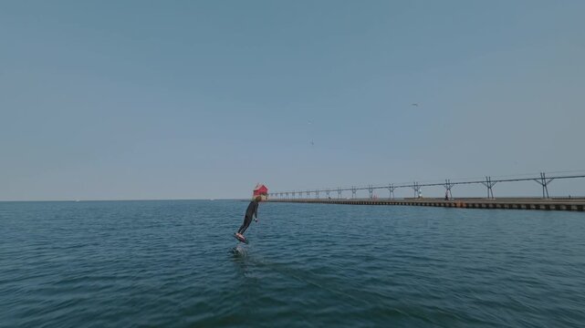 Surfer performing aerial trick on electric hydrofoil board near a lighthouse