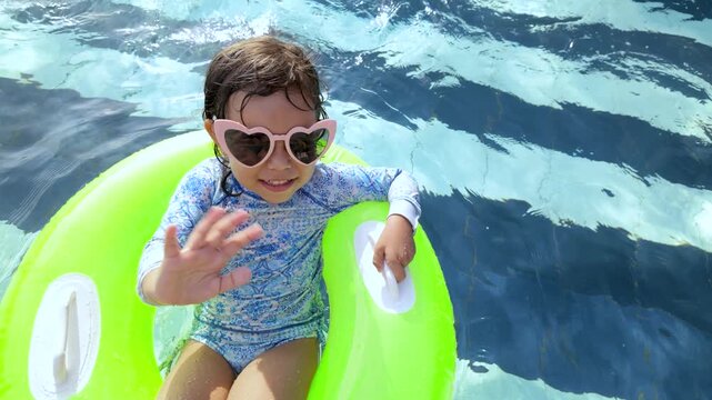 Little girl having fun swimming in inflatable ring wearing sunglasses at resort pool - Travel summer vacation