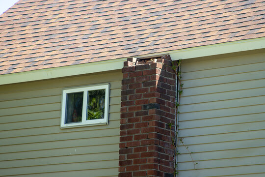 A brick chimney in need of repair on the side of a two-story wooden house