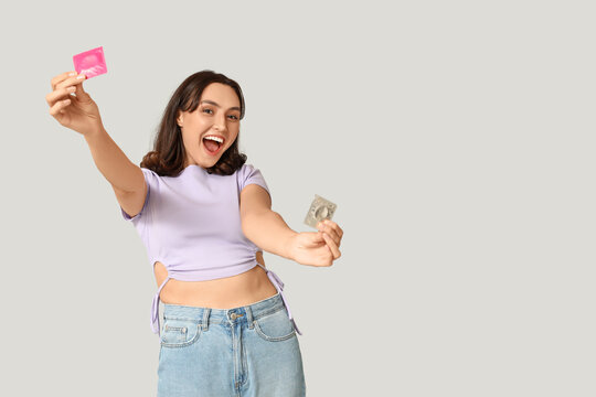 Happy young woman with condoms on grey background. Safe sex concept