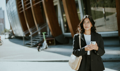 Fototapeta premium Woman standing on street with phone outside modern building in urban setting