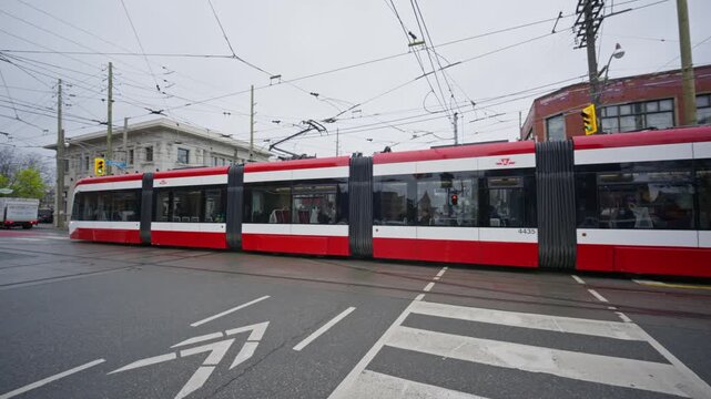 Iconic red streetcar navigating busy intersection in Toronto, Canada, with complex overhead power lines and modern architecture on overcast day