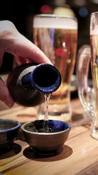 A Person Pouring Japanese Sake From a Ceramic Bottle Into a Cup