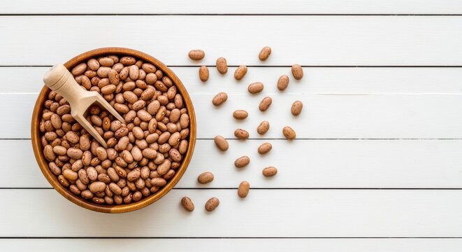 Bowl of pinto beans with a wooden scoop on a white wooden background