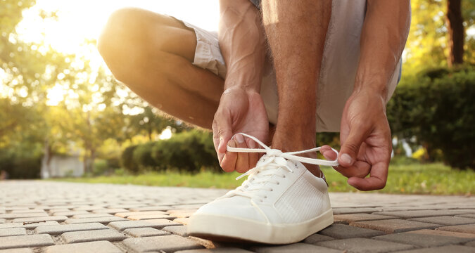 Sporty young man tying shoe laces outdoors