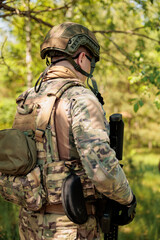 Obraz premium A soldier in a helmet, body armor, and with a machine gun stands sideways in the forest