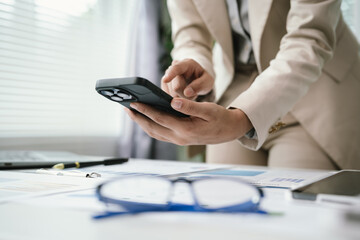 Fototapeta premium Close-up of a business professional using a smartphone while reviewing financial documents at a modern office desk, highlighting mobile communication, productivity, and digital workflow.