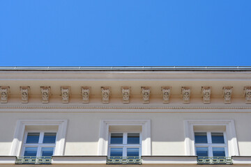 Low angle view of a nineteenth century historic building roofline with an ornate decorative cornice and classical windows under a clear blue sky in Zagreb, Croatia. © nahhan