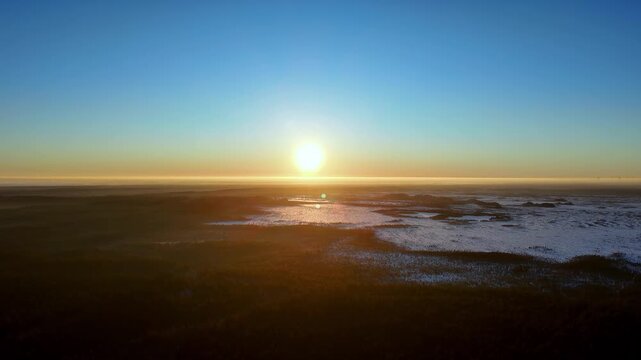 A Breathtaking Golden Hour High Angle Drone Shot Of A Frozen Winter Tundra In Iceland During A Clear Sunset Showing Vibrant Blue Skies And Warm Orange Sun Rays Reflecting Over Icy Plains And Snow Fiel