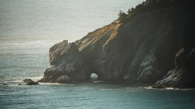 Cannon Beach, close up of rocky coastal cliff with natural arch over ocean water under soft daylight conditions