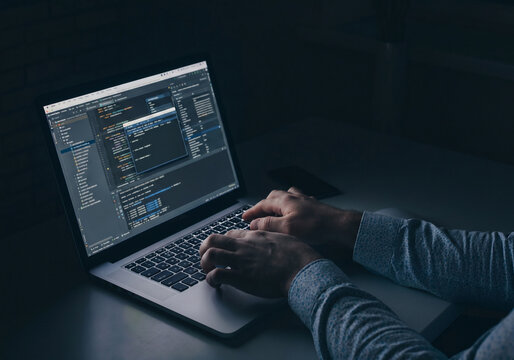Person working on computer in dark room while coding software at night