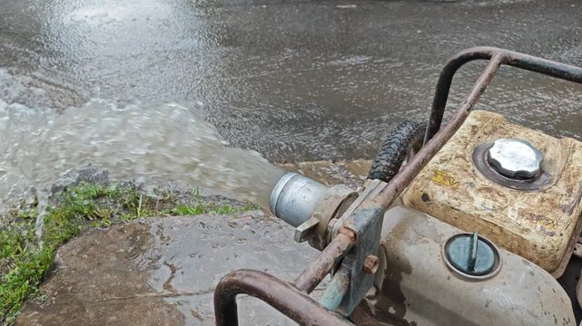 A portable gas motor pump actively pumping and discharging a powerful stream of muddy water onto the pavement