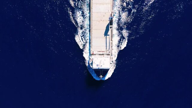 High-angle drone footage capturing the detailed white water wake trailing behind a large cargo vessel in the deep blue ocean.