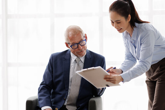 Businesswoman discussing document details with male executive, providing guidance and showing information on a clipboard during a corporate meeting in a modern office setup