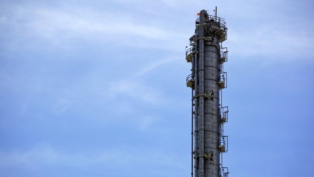 Tall Insulated Distillation Column Tower With Access Platforms Against Cloudy Sky
