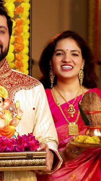 Indian Couple Welcoming Ganesh Idol with Joy, Young husband wife in Traditional Attire Holding Ganpati Bappa Idol, Puja Thali While Smiling and Chanting Bappa Morya During Ganesh Festival Celebration