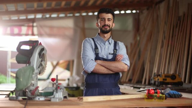 A man in a blue jumpsuit stands in front of a table with a saw and other tools