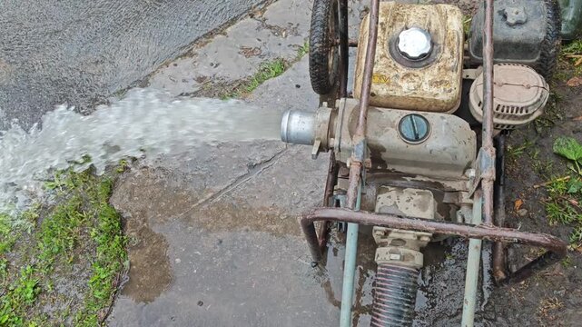 High angle shot of a portable gas motor pump discharging a powerful stream of dirty water onto the pavement during utility repair works
